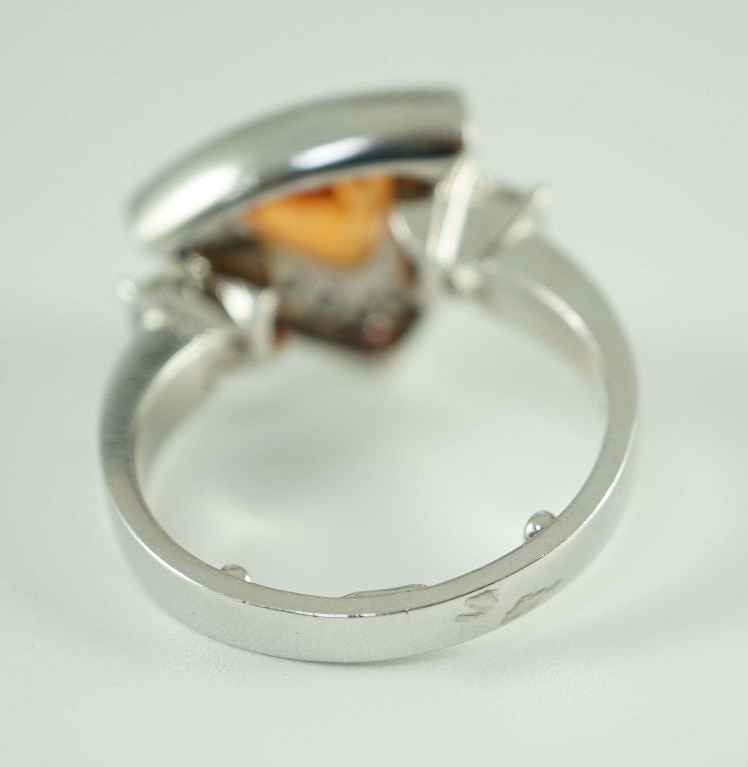 A modern platinum and single stone trilliant cut spessartite garnet ring, with diamond set border and two criss-emerald cut diamond set shoulders, by Musson